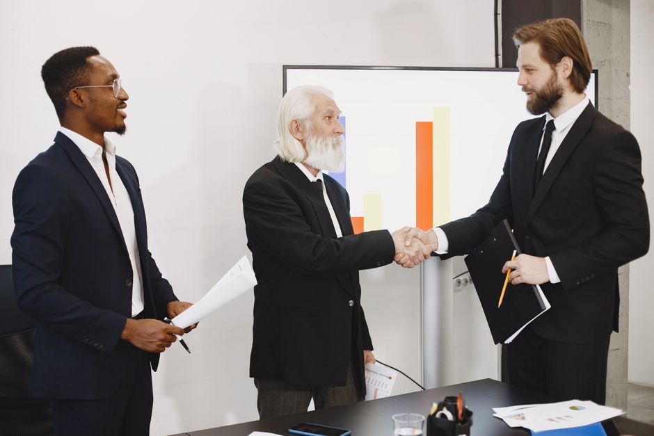 Three businessmen in suits having a meeting, shaking hands in front of a presentation chart.