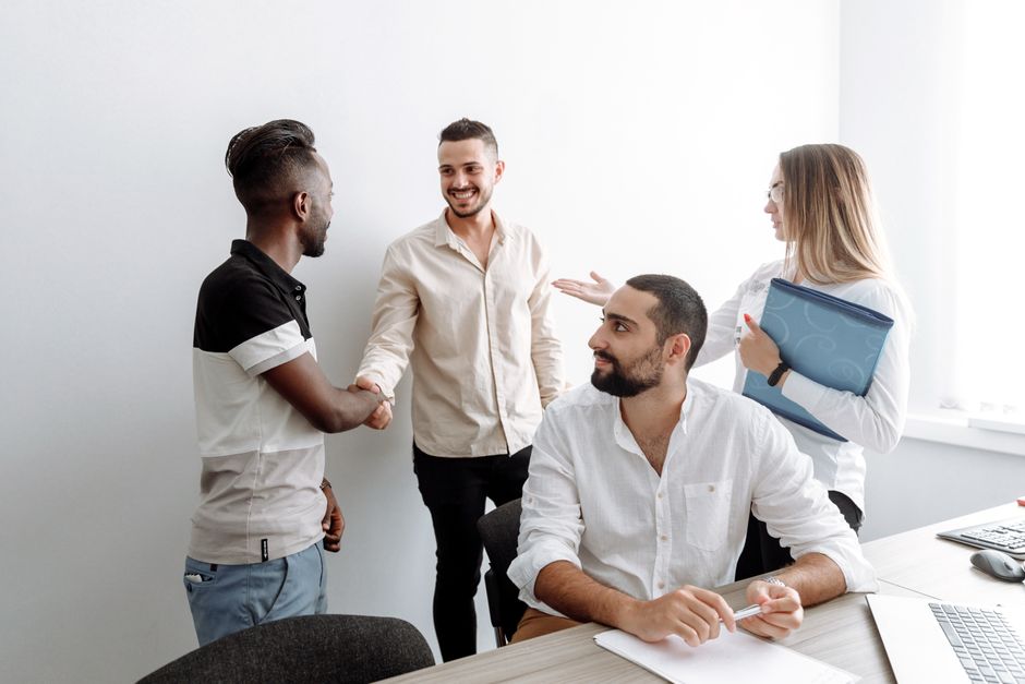 A team of diverse professionals shaking hands and smiling in an office setting, symbolizing cooperation.